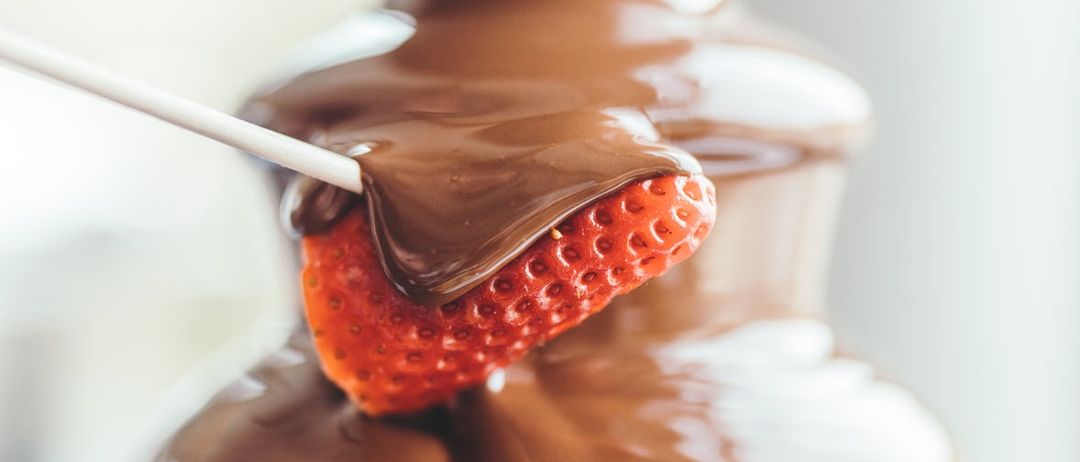 Eine Erdbeere wird in eine Schokoladenfontäne getaucht, wobei das schmelzende Schokolade um die Frucht herum sichtbar ist.