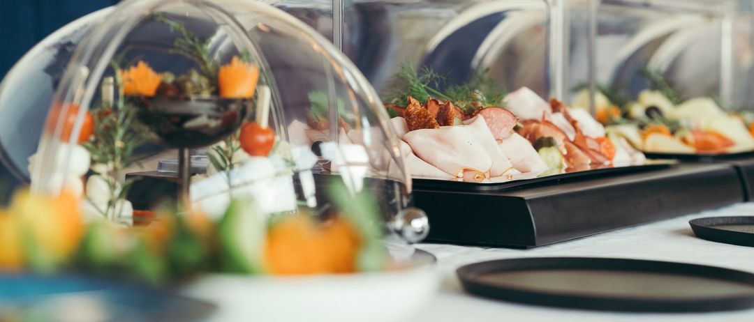 Ein Tisch mit verschiedenen Speisen unter Glaskuppeln. Die Speisen bestehen aus Fleisch, Gemüse und Garnierungen.