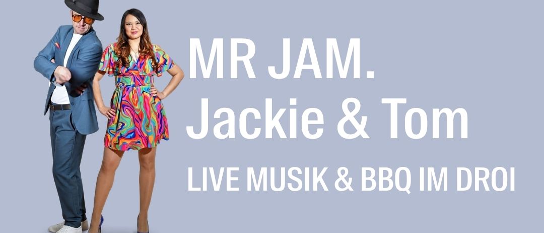 Ein Mann und eine Frau stehen eng nebeneinander vor einem grauen Hintergrund. Der Mann trägt einen Anzug und Hut, die Frau ein farbenfrohes Kleid. Der Text lautet 'MR JAM. Jackie & Tom LIVE MUSIK & BBQ IM DR0I'.