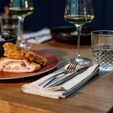 Eine Holztisch-Einrichtung mit einem Teller frittierter Hähnchen, einem Glas Wein und einem Glas Wasser.