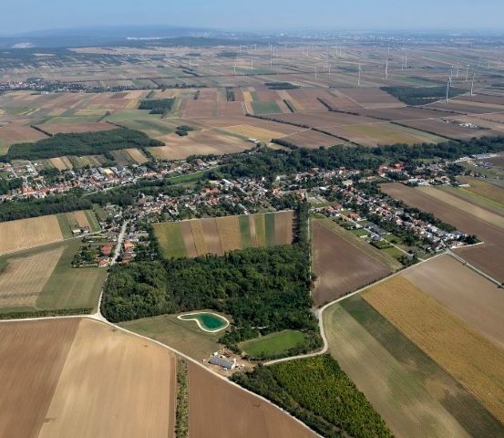 Eine Luftaufnahme eines ländlichen Gebiets mit mehreren Feldern und einer kleinen Stadt, umgeben von Grünflächen und Windrädern.