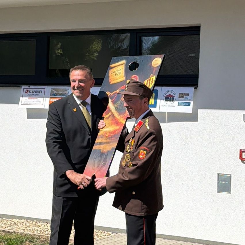 A man in formal attire presents a plaque to a uniformed individual outside a building.