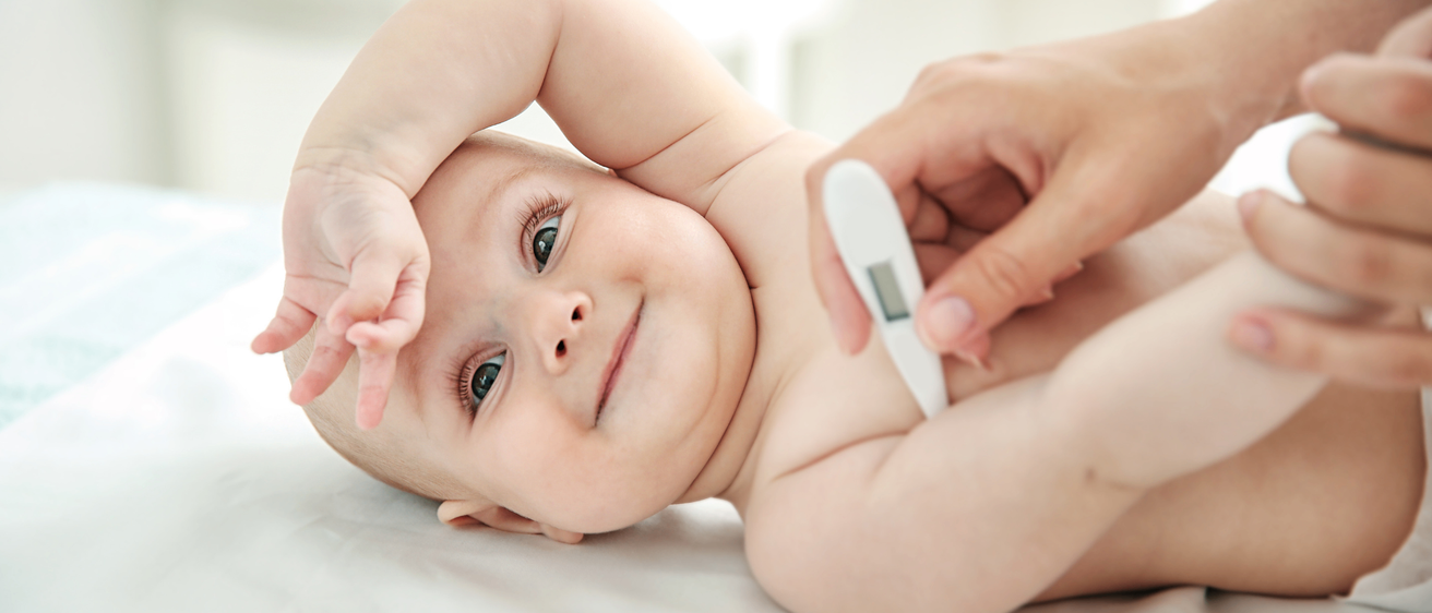 Ein Baby, das auf einem Bett liegt, hat seine Temperatur mit einem digitalen Thermometer von einem Erwachsenen gemessen.