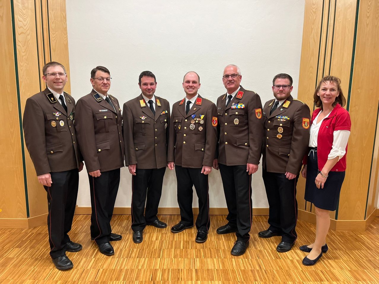 Eine Gruppe von sieben Personen, sechs Männer und eine Frau, in identischen Militäruniformen gekleidet, posiert für ein Foto in einem Raum.