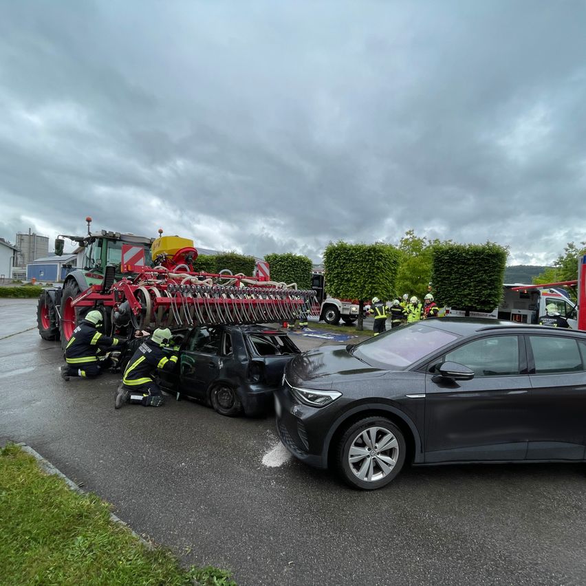 Emergency responders are working on a car accident involving a tractor and a car on a road under a cloudy sky.