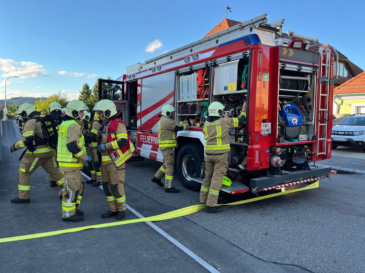 Firefighters are preparing their truck for a mission. They are in full uniform, standing around the truck. The truck is parked on the side of the road.