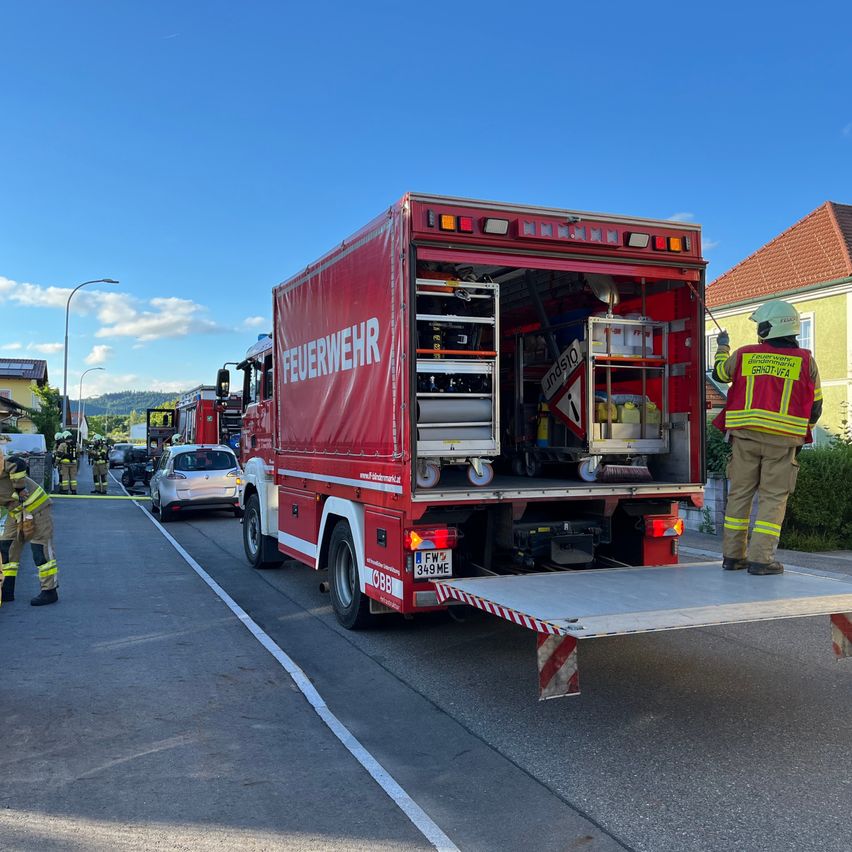 A red fire truck with the text 'Feuerwehr' on its side is parked on the side of the road. A firefighter is standing beside it.