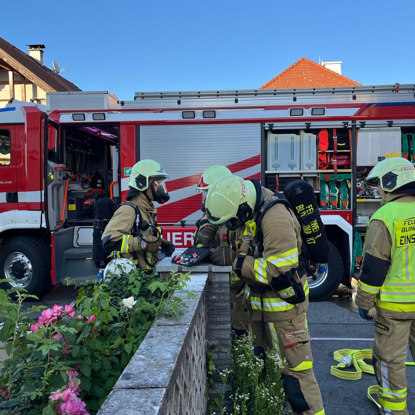 Firefighters stand near a fire truck, preparing for a task with flowers in the background.