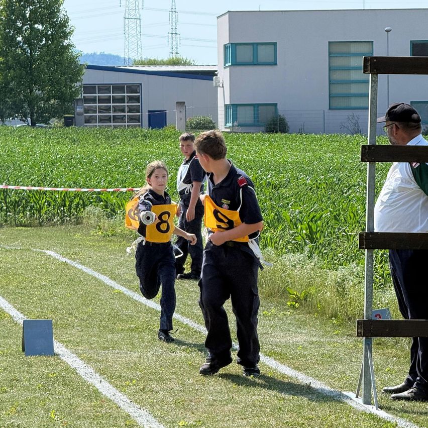Ein junges Mädchen läuft auf einem Rasenfeld mit drei Jungen und einem Mann, der zusieht. Der Junge vorne trägt ein gelbes Trikot mit der Nummer 8.