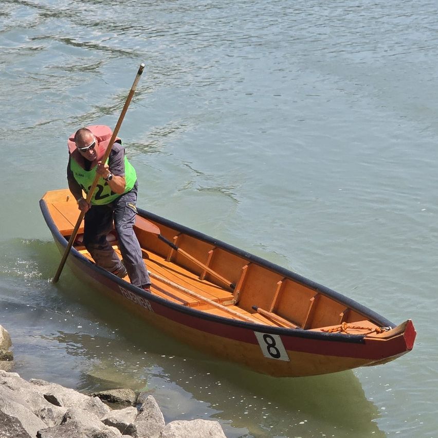 Ein Mann rudert in einem Fluss. Er trägt eine Schwimmweste und hält ein Paddel. Das Kanu ist mit der Nummer 8 gekennzeichnet.