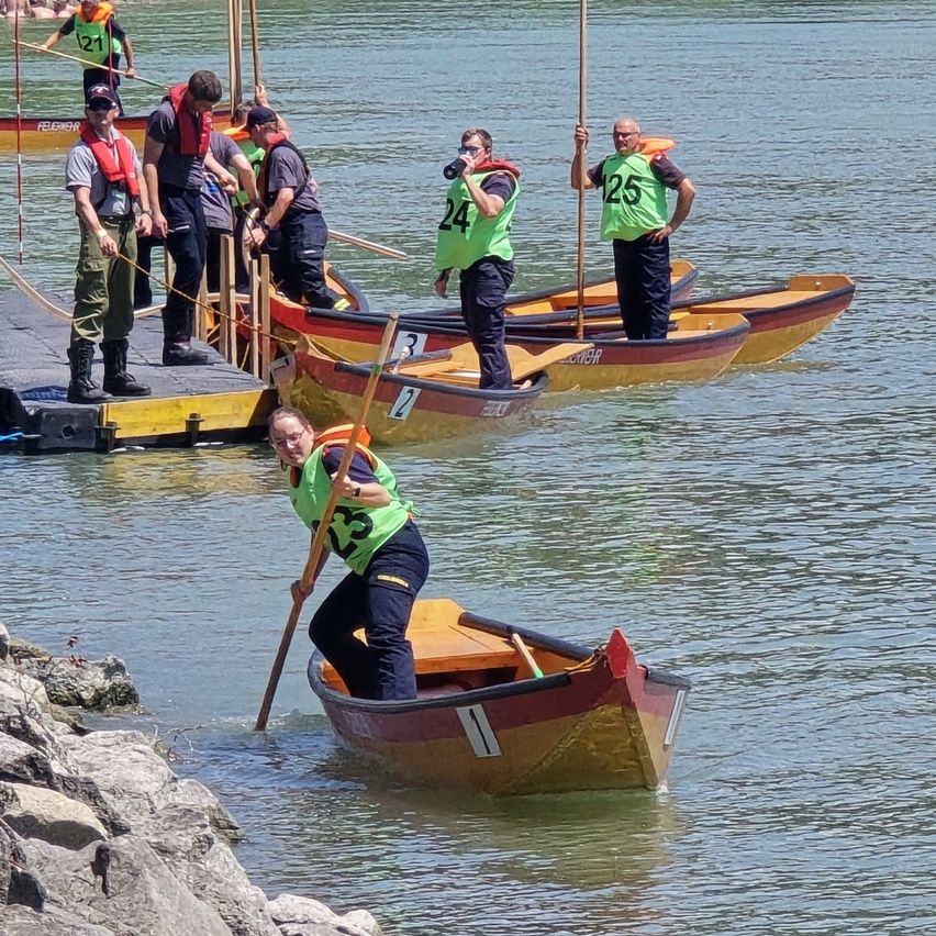 Eine Gruppe von Menschen in grünen Westen und Mützen bereitet sich darauf vor, ihre Boote auf einem ruhigen Fluss zu rudern. Sie stehen auf einem Steg.