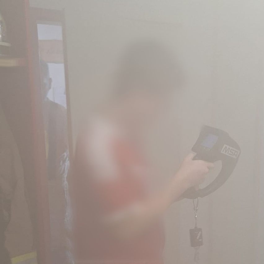 Ein verschwommenes Bild zeigt eine Person, die ein Gerät mit 'MSA' davor hält, vor einer verhangenen Wand.