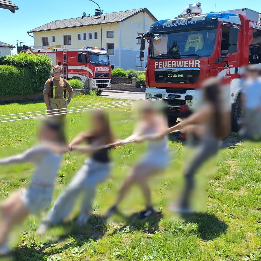 Ein Feuerwehrmann beobachtet, wie Kinder an Seilen ziehen, mit einem Feuerwehrfahrzeug im Hintergrund.