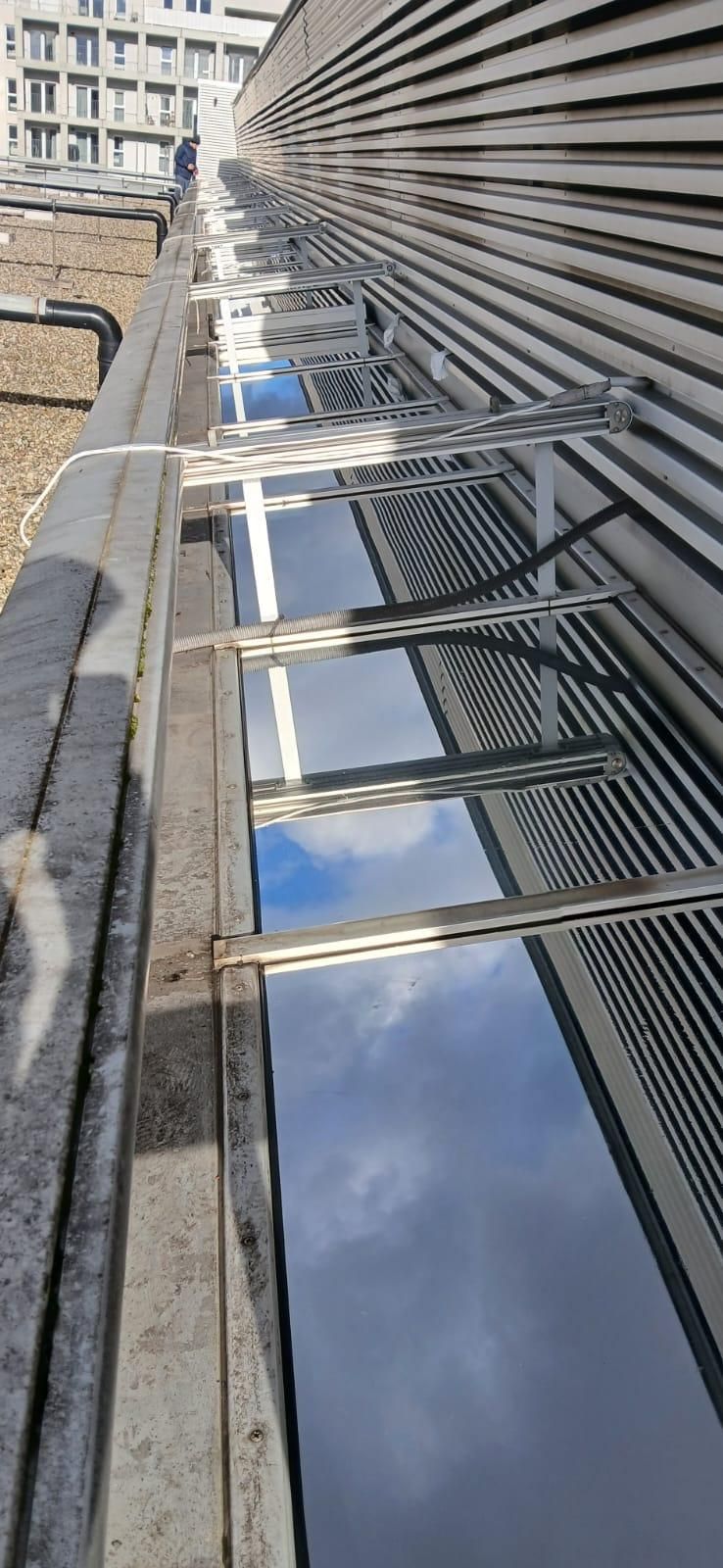 Eine Nahaufnahme eines Glasfensters eines Gebäudes mit Metallrahmen, das den Himmel und Wolken reflektiert.