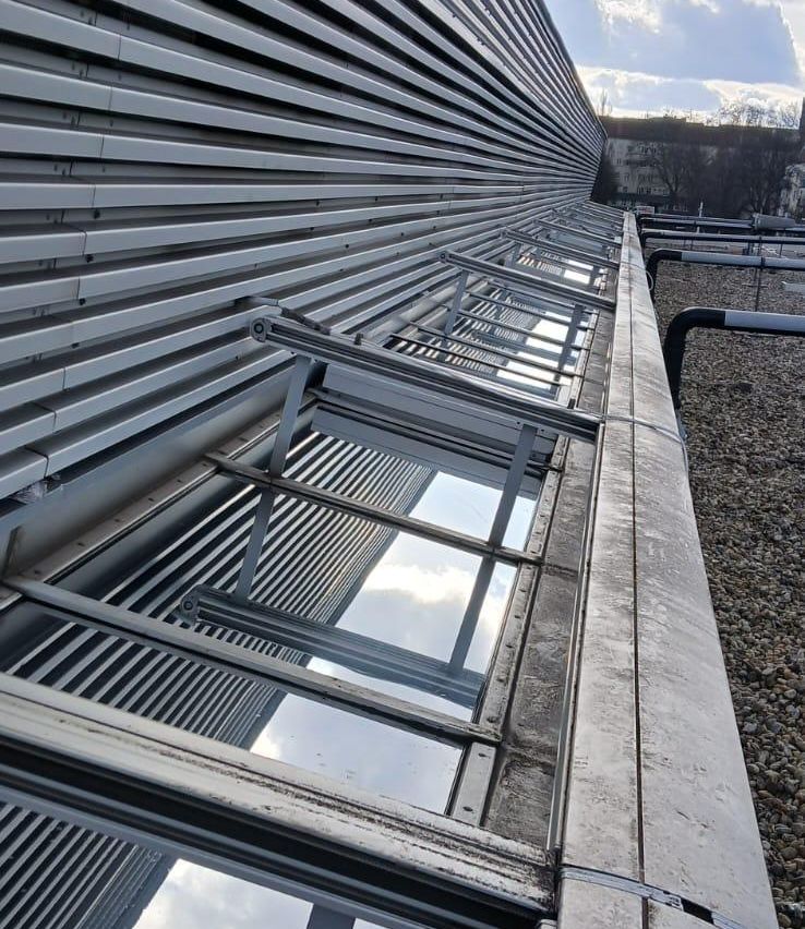 Nahaufnahme der Außenseite eines Gebäudes mit einer Reihe rechteckiger, metallischer Fenster. Die Fenster sind geöffnet und reflektieren den Himmel und die umliegenden Strukturen.