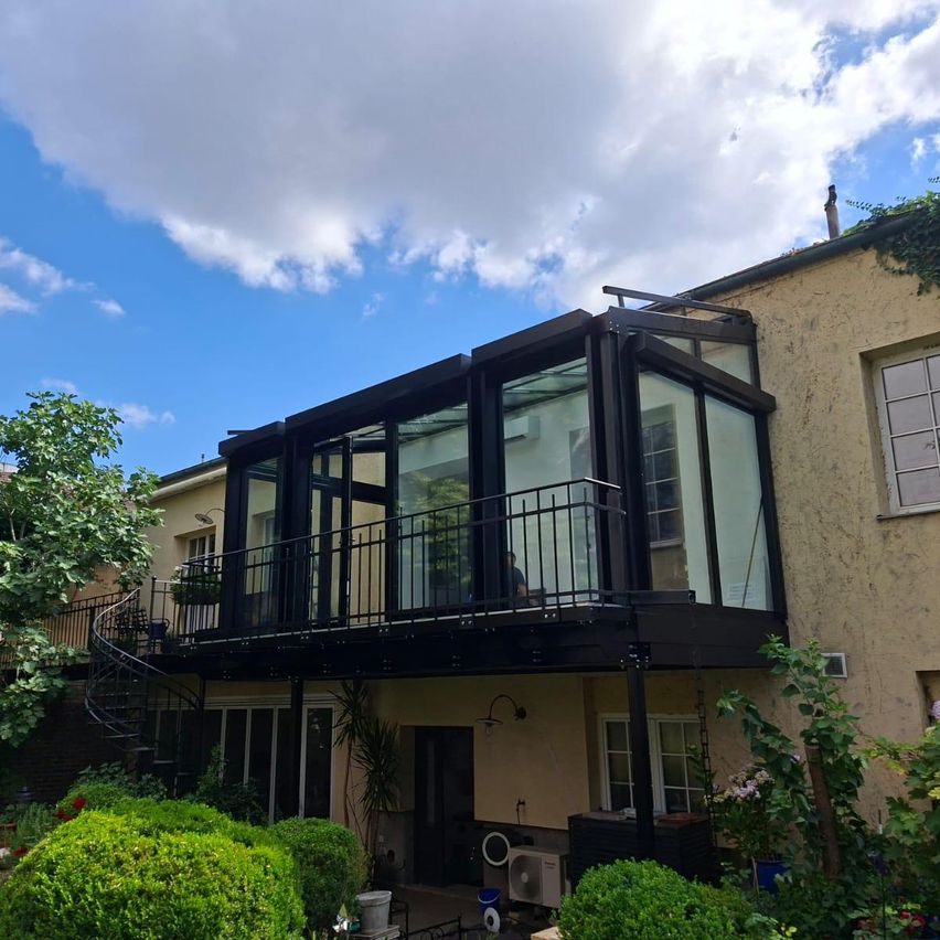 A modern house with a glass balcony and spiral staircase under a partly cloudy sky.