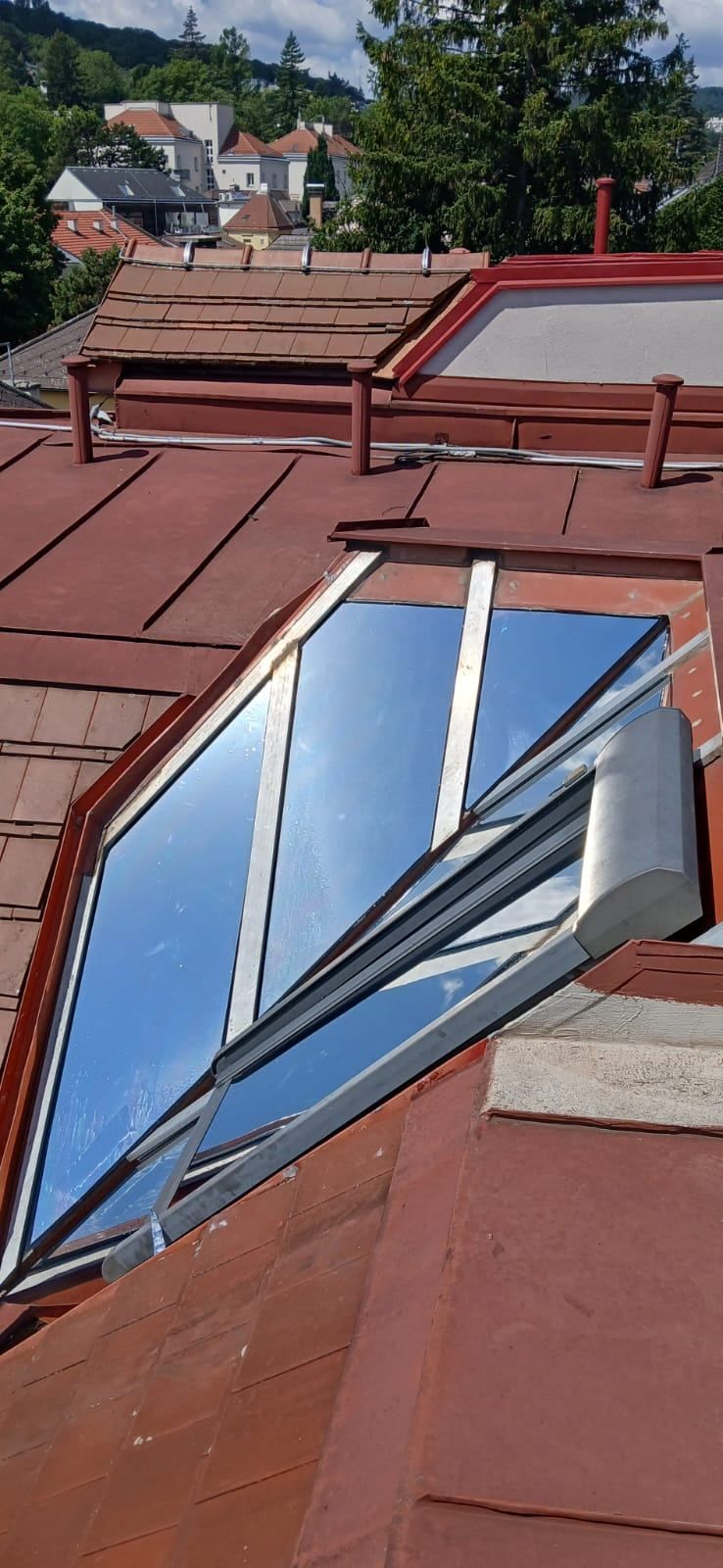 A close-up view of a red roof with a glass window that is open. The window has a silver frame and a metal handle. The sky is visible through the window.