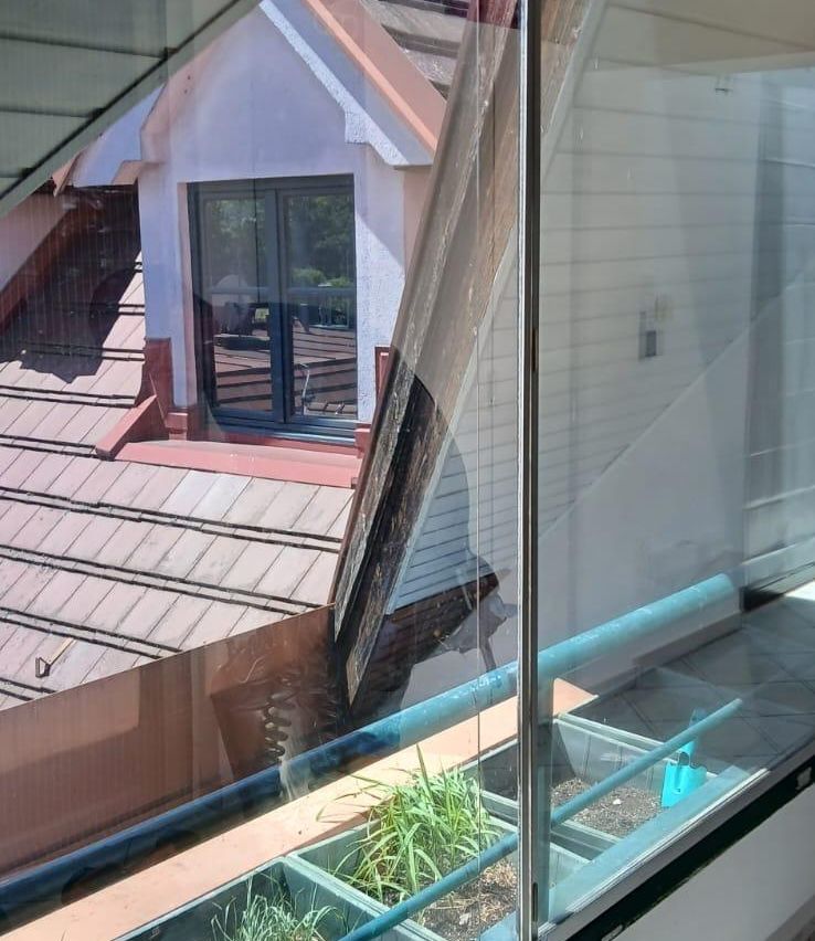 A view from a window showing a house with a red roof and a glass window with a reflection of trees and a building.