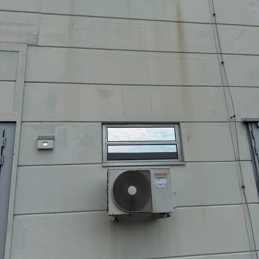 A white building with a window and an air conditioning unit mounted on the wall.