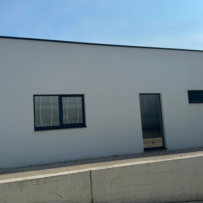 A modern white building with a glass door and two windows with black frames under a clear blue sky.
