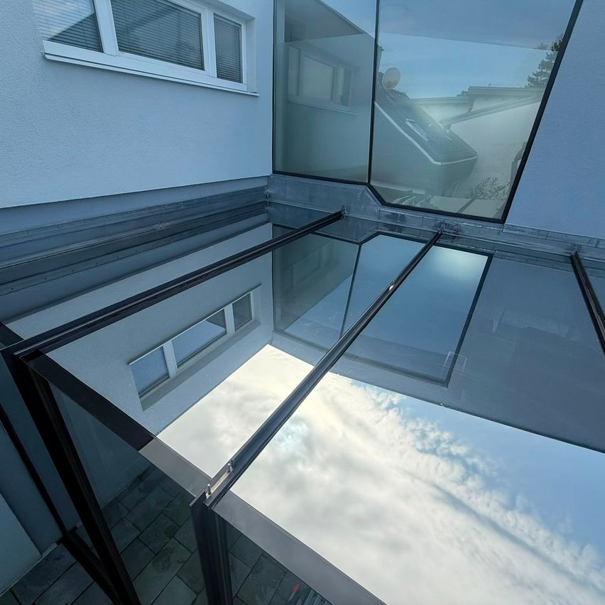 A modern glass roof extension with a view of a cloudy sky and a house in the background.