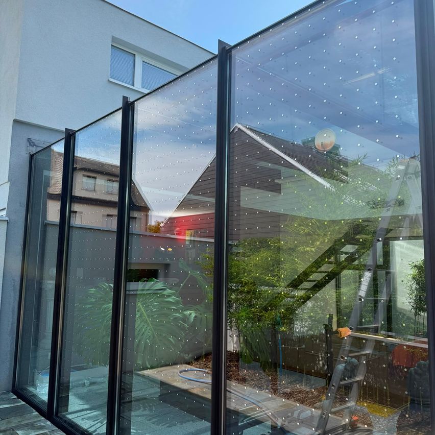 A modern glass fence with a dotted pattern is installed in front of a house with a staircase leading to a patio.