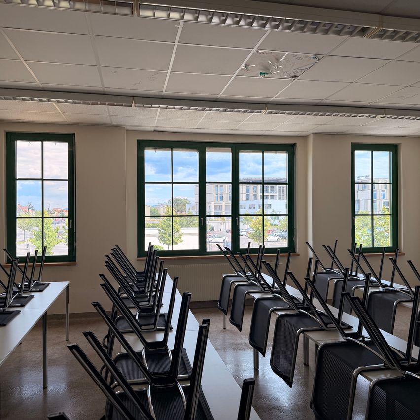 An empty classroom with rows of chairs facing the windows, showing a view of the city outside.