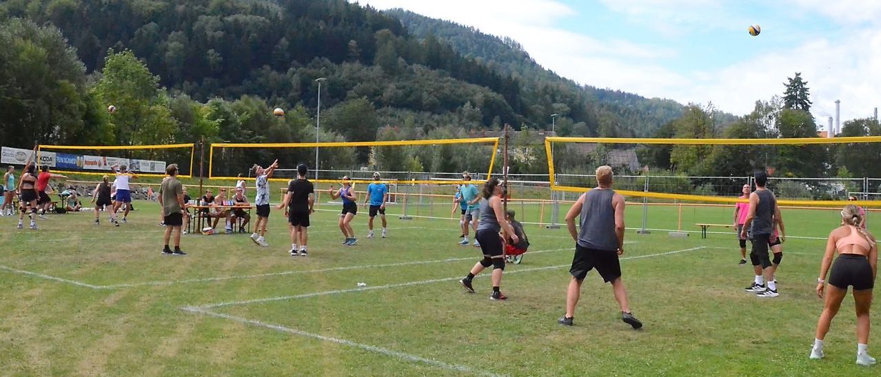 Eine Gruppe von Menschen spielt Volleyball auf einem Rasenfeld mit einem Berg im Hintergrund.