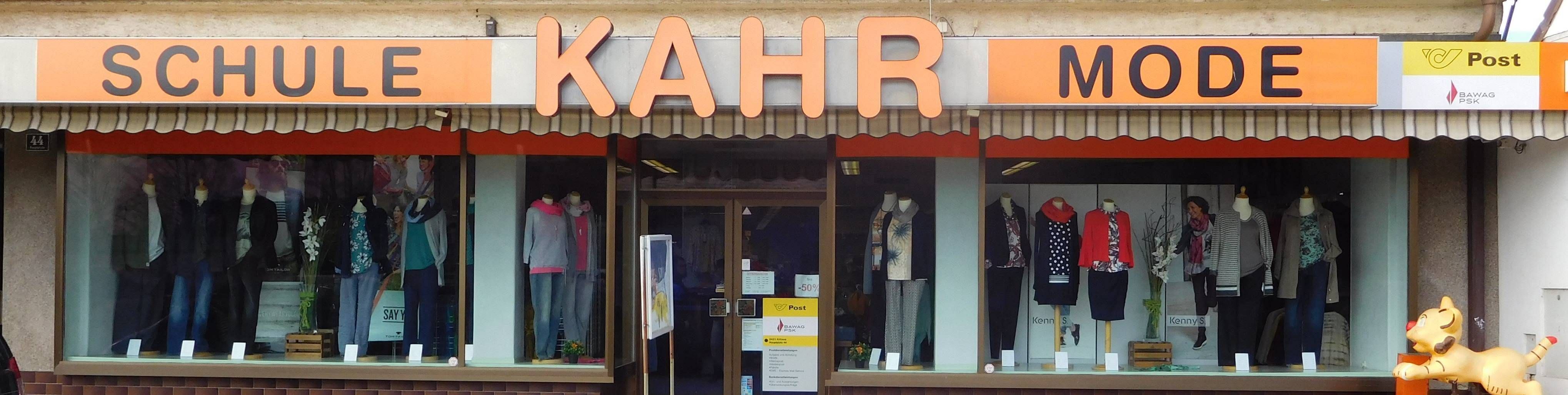 Ein Laden mit orangefarbenen Buchstaben, die 'KAHHR' über dem Eingang bilden. Im Inneren befinden sich in Kleidung gekleidete Mannequins und ein Schild mit gelbem Hintergrund und schwarzem Text.