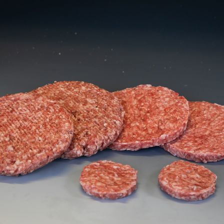 Mehrere rohe Hamburger-Patties sind auf einer dunklen Oberfläche angeordnet. Die Patties variieren in der Größe, wobei einige größer und andere kleiner sind. Sie sind roh und sehen frisch aus.