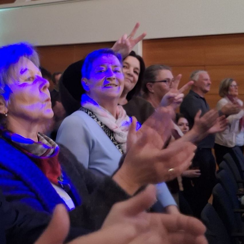 Eine Gruppe von Menschen klatscht und lächelt in einer Innenumgebung. Einige von ihnen haben blaue Lichter auf ihren Gesichtern.