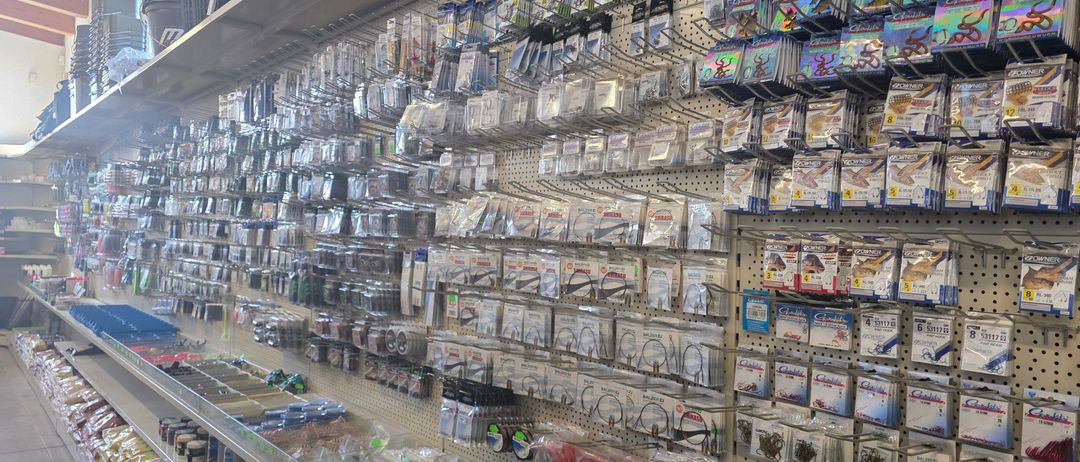 Ein Geschäft mit einer großen Auswahl an Angelzubehör, Haken, Köder und Köder. Die Regale sind gefüllt mit verschiedenen Packungen und Kisten, einige mit grünen Etiketten.