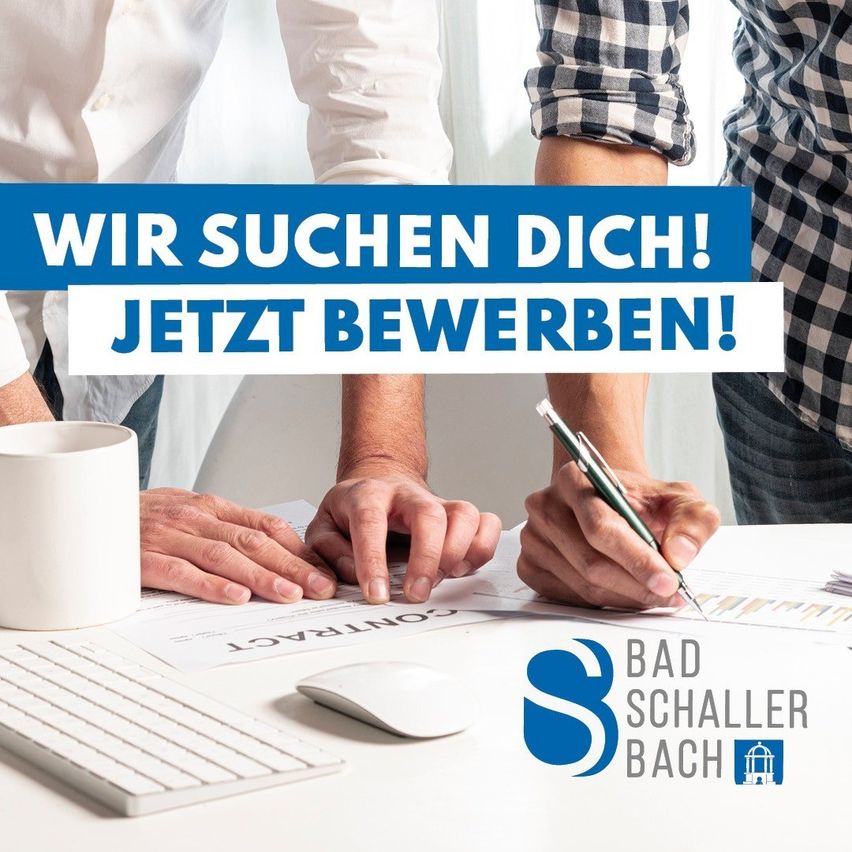 Drei Personen stehen um einen Schreibtisch mit Papieren, einer Tastatur und einer Kaffeetasse. Sie schreiben auf einem Blatt Papier. Ein blaues Schild mit weißen Texten sagt 'Wir suchen Dich! Jetzt bewerben!' Ein Logo befindet sich unten rechts.