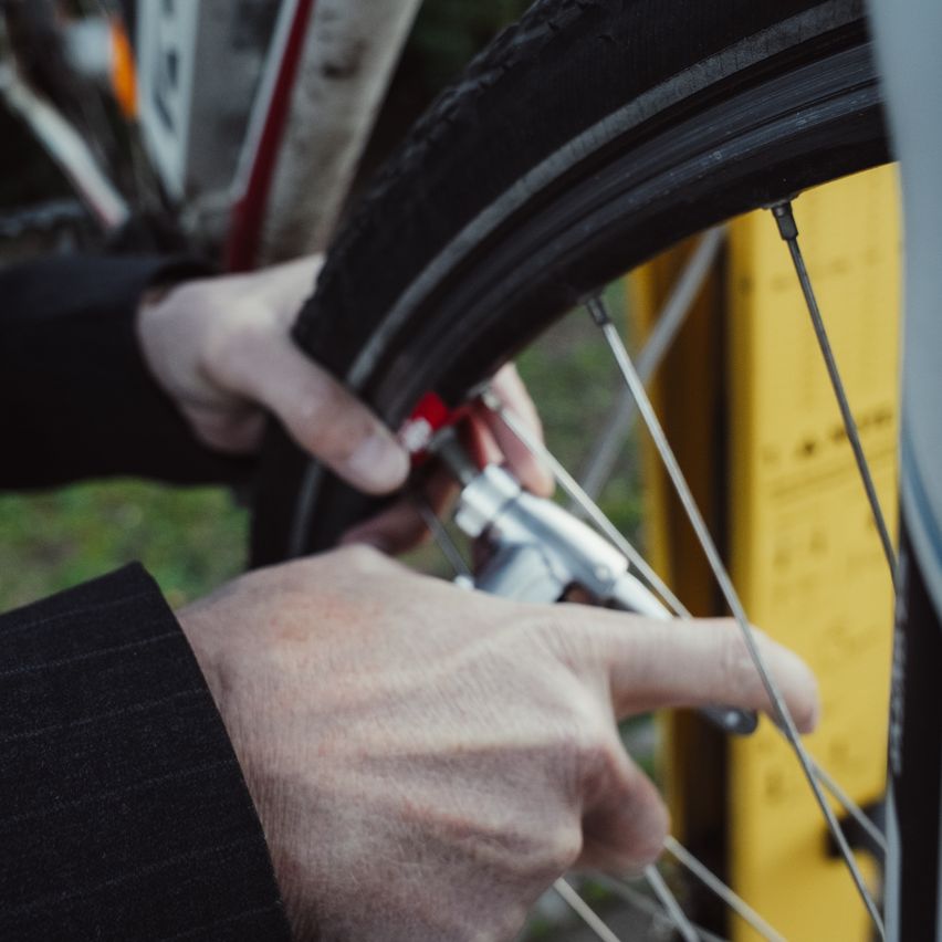 Eine Person repariert das Rad eines Fahrrads mit einem Werkzeug. Das Fahrrad steht auf Gras, und die Person trägt ein schwarzes Langarmhemd.