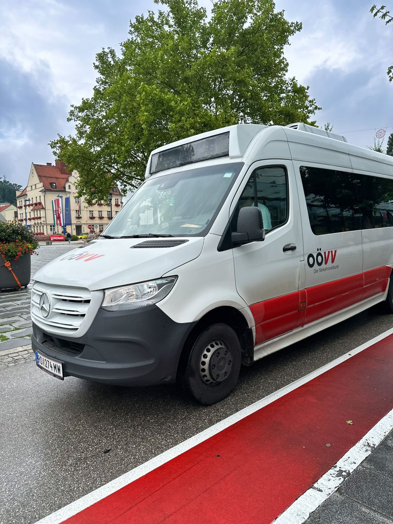 Ein weißer und roter Mercedes-Benz Sprinter Minibus ist auf einer Straße mit einem roten Fahrradstreifen geparkt. Der Minibus hat den Text 'oovv' an seiner Seite.
