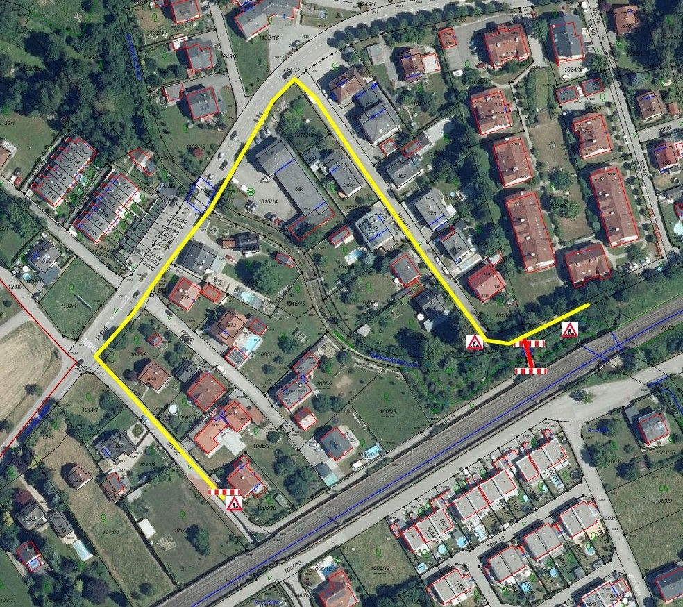 Eine Luftaufnahme eines Vororts mit Wohngebäuden, Straßen und einer Eisenbahnstrecke. Das Gebiet ist mit gelben Linien und roten Rechtecken markiert, die Grenzen und Zonen anzeigen. Bäume und Grünflächen sind im gesamten Gebiet sichtbar.