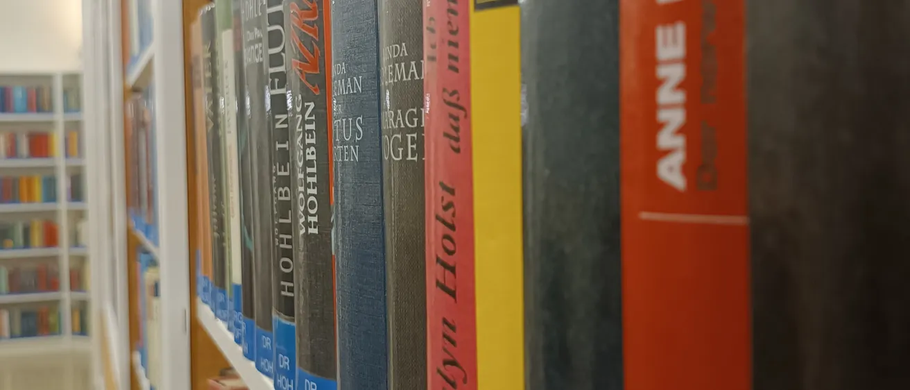 Ein Bibliotheksgang gefüllt mit Büchern, darunter Titel von Dr. Hoch, Dr. Hol und Dr. P. Die Bücher sind in Reihen auf Regalen angeordnet.