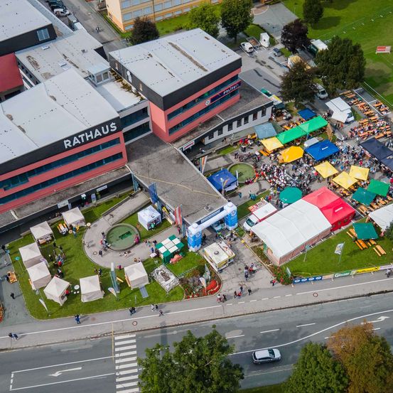 Luftaufnahme eines Events beim Rathaus mit vielen Zelten und Menschen. Das große Gebäude im Hintergrund trägt den Schriftzug Rathaus. Mehrere Fahrzeuge sind geparkt und eine Straße verläuft durch das Gebiet.