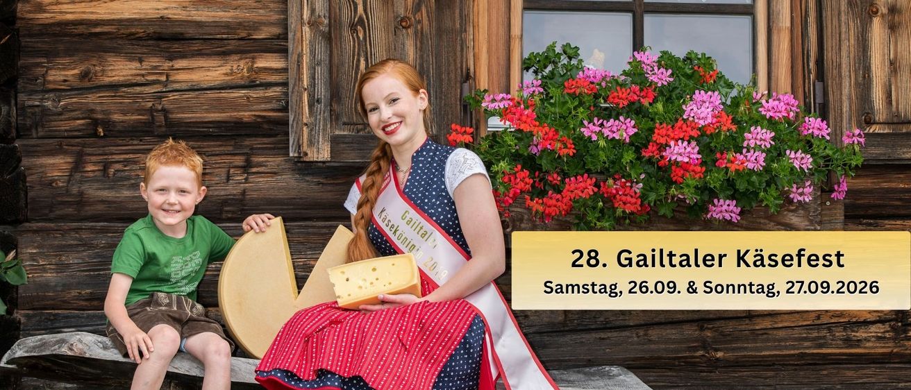 Eine Frau und ein Junge sitzen auf einer Holzbank vor einem Holzhaus. Die Frau hält ein Stück Käse und lächelt. Der Junge hält auch ein Stück Käse. Es gibt ein Fenster mit einer Pflanze auf der Fensterbank.
