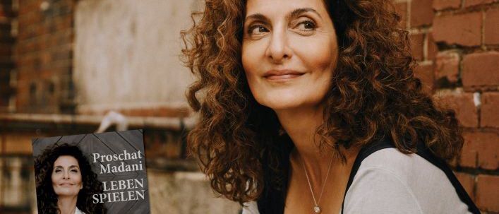 Eine Werbung für Proschat Madanis Buch 'Leben Spielen' zeigt eine lächelnde Frau mit lockigem Haar, die gegen eine Backsteinmauer lehnt. Das Buchcover zeigt eine ähnliche Frau in einem weißen Hemd. Der Text lautet 'Proschat Madani Leben Spielen' und das Datum 'FR. 20. MÄRZ 2026'.