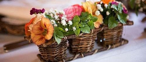 Drei kleine Korbkörbe voller bunter Blumen stehen auf einem Tisch. Die Blumen sind in einer Reihe angeordnet.
