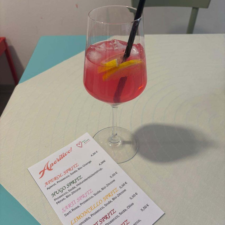 Ein Weinglas mit einem rosa Getränk und Zitronenscheibe auf einem Tisch mit einer Speisekarte davor.