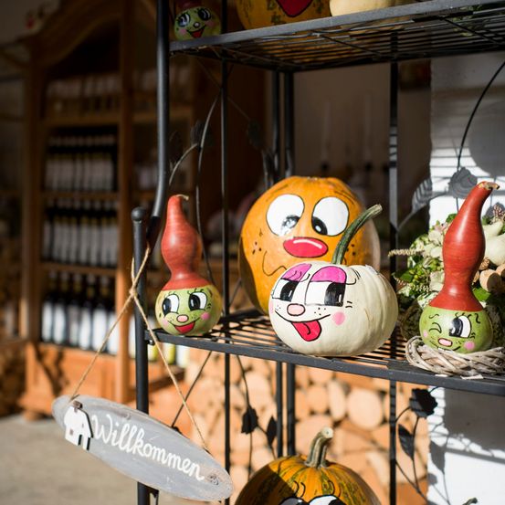 Ein schwarzes Regal mit verschiedenen handbemalten Kürbissen mit Gesichtern, darunter ein orangefarbener Kürbis mit roter Nase und rosa Wangen, ein grüner Kürbis mit rosa Nase und Wangen und ein roter Kürbis mit grünen Wangen.