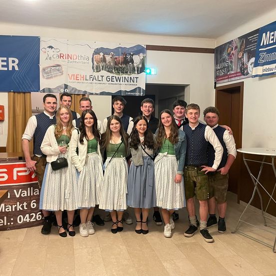 Eine Gruppe junger Leute in traditioneller Kleidung, die zusammenstehen und für ein Foto in einem geschmückten Raum lächeln.