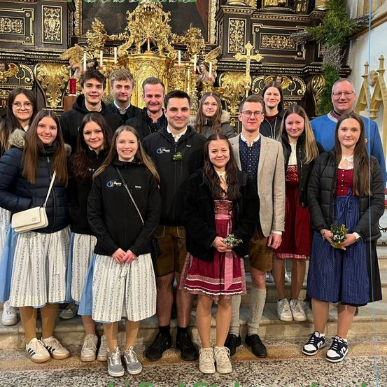 Eine Gruppe von Menschen, wahrscheinlich eine Familie oder ein Team, posiert für ein Foto vor einem Altar. Sie sind in verschiedenen Winterkleidung gekleidet, einige mit Blumenzubehör.