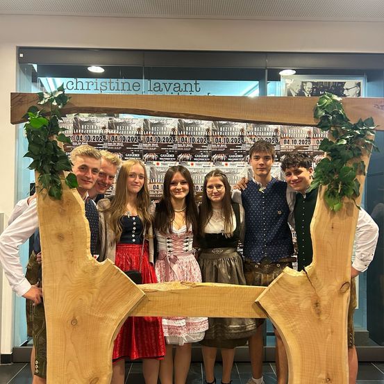 Eine Gruppe junger Menschen in traditioneller deutscher Kleidung posiert für ein Foto in einem Holzrahmen in einem Museum.