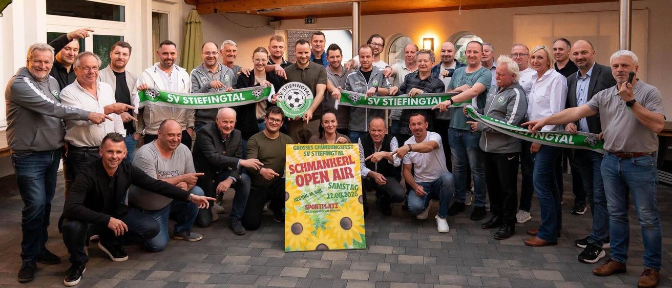 Gruppenfoto mit Bannern, Menschen, die ein Band halten, und ein Schild für ein 'Schmanhere Open Air' Event am Samstag.
