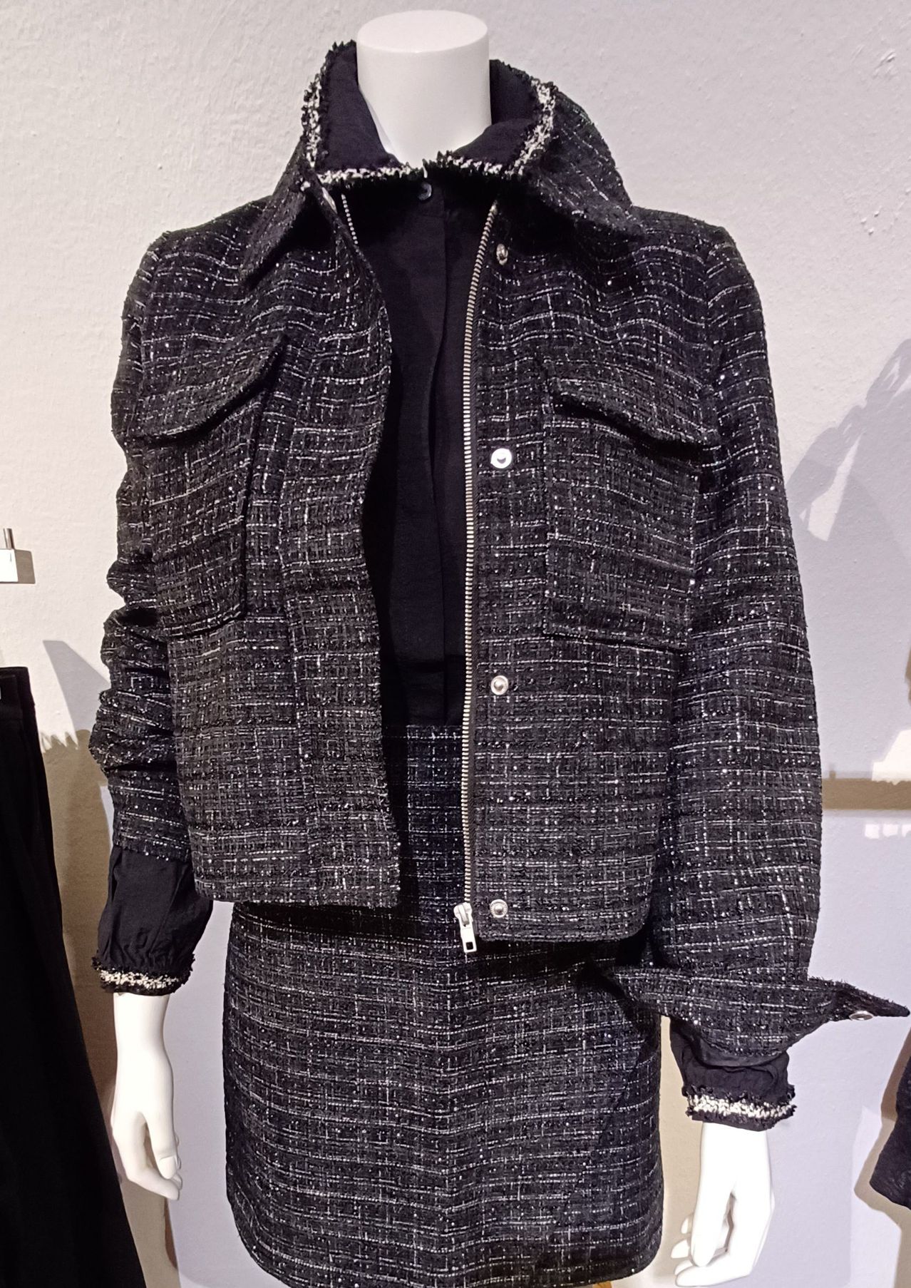 Eine Puppe trägt eine schwarz-weiß karierte Jacke mit Reißverschluss und passendem Rock, vor weißem Hintergrund präsentiert.