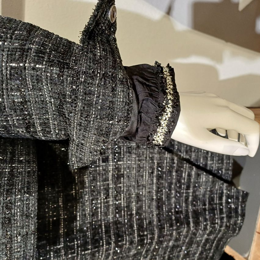 Eine Nahaufnahme des Arms einer Puppe, die ein schwarzes und silbernes Paillettenkleid mit goldener Spitzenkante am Ärmel trägt.
