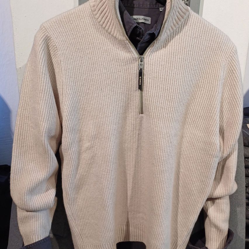 A beige ribbed sweater with a zipper by Jack & Jones, hanging on a hanger.